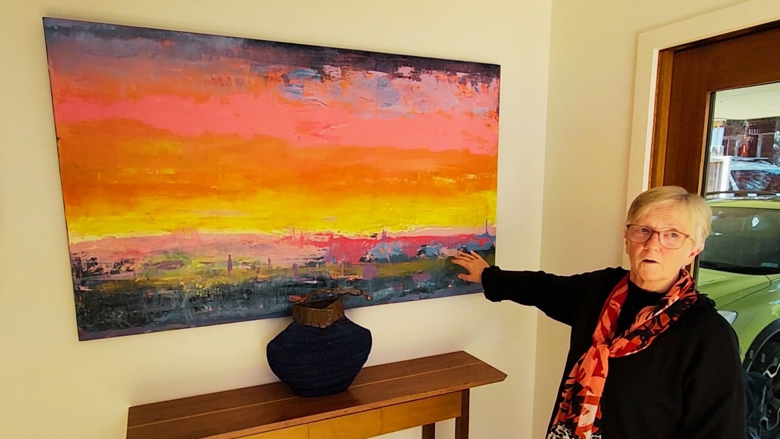 Local artist Deb standing next to a colourful abstract painting hung on a wall in her home, illustrating the successful art hanging service provided by Cinnamon.