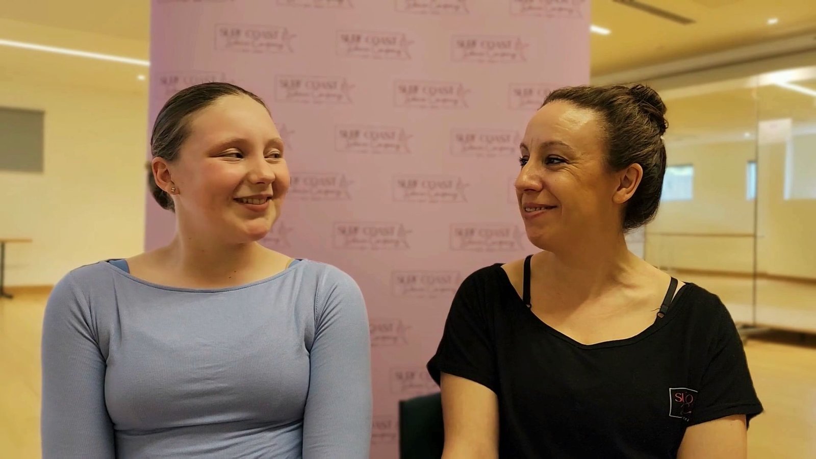 Surfcoast Dance Company student Emma (left) and owner Miss Melinda (right) sitting together and smiling in Torquay, discussing Emma's dance experience.