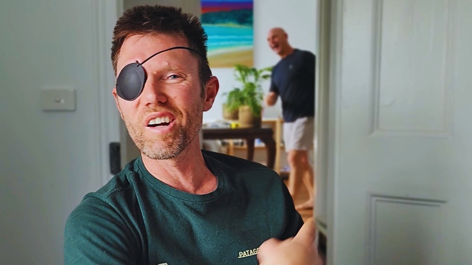 Club member Ryan, wearing an eyepatch and a green shirt, speaks positively to the camera about his recovery journey, while founder Tim Altman laughs warmly in the background inside Sublime Health Club.